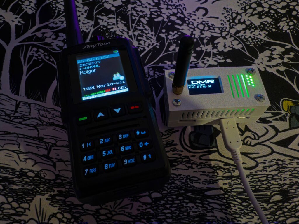 Radio and DMR hotspot on a desk, both lit up and displaying a callsign transmitting.